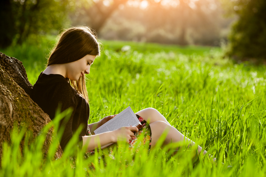 Teenage girl reading book in meadow