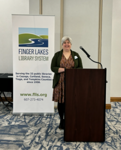 Finger Lakes Library System Executive Director Sarah Glogowski smiles in front of a podium