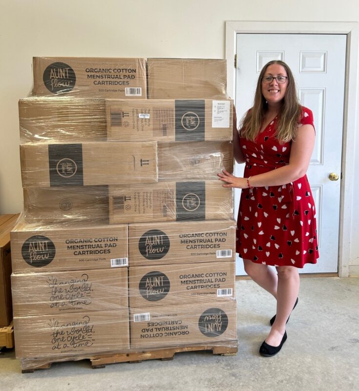 woman in a red dress standing next to many boxes of tampons and pads