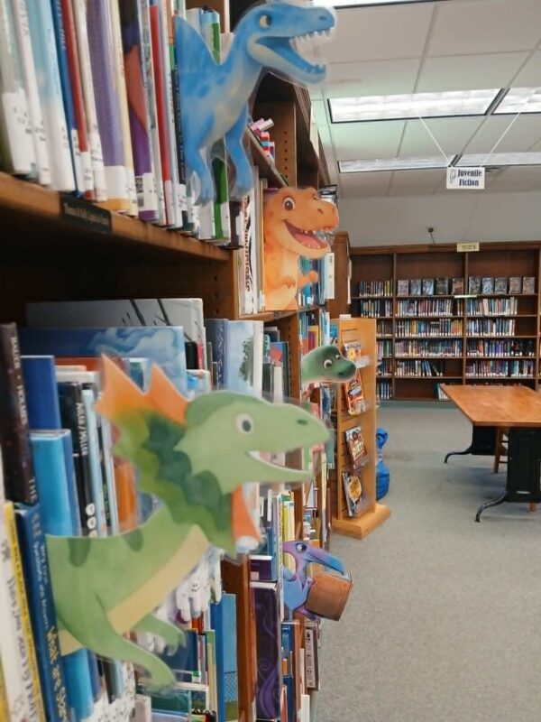 Paper dinosaurs pop out from the library stacks