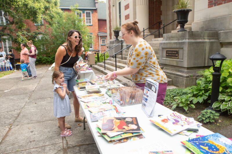 a library staff member hands out books to a parent and child